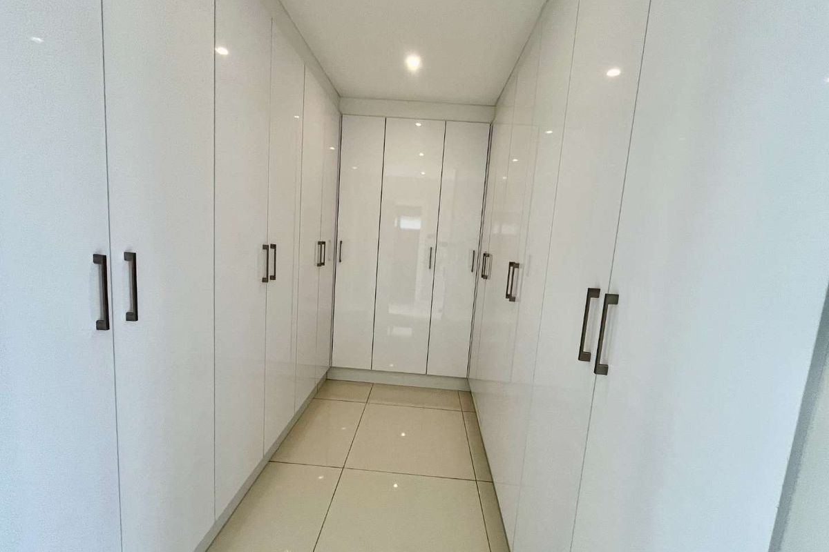 A modern walk-in dressing area featuring extensive floor-to-ceiling white high-gloss cabinetry and polished tiled flooring.