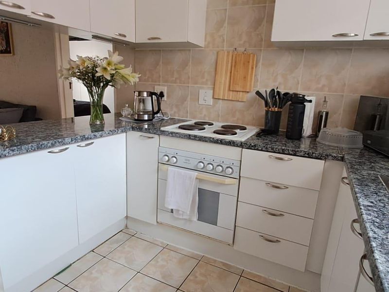 A functional kitchen featuring white cabinetry, granite countertops, a built-in oven with electric hob, and tiled flooring.