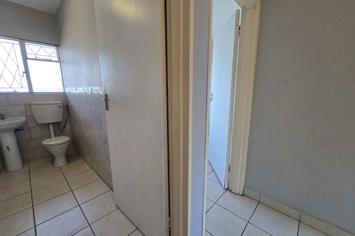 A functional bathroom featuring a pedestal sink, toilet, and tiled finishes, currently vacant and ready for renovation or updates.
