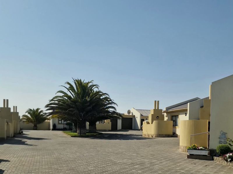 A view of the townhouse complex entrance featuring a paved driveway, established palm trees, and masonry architectural details.