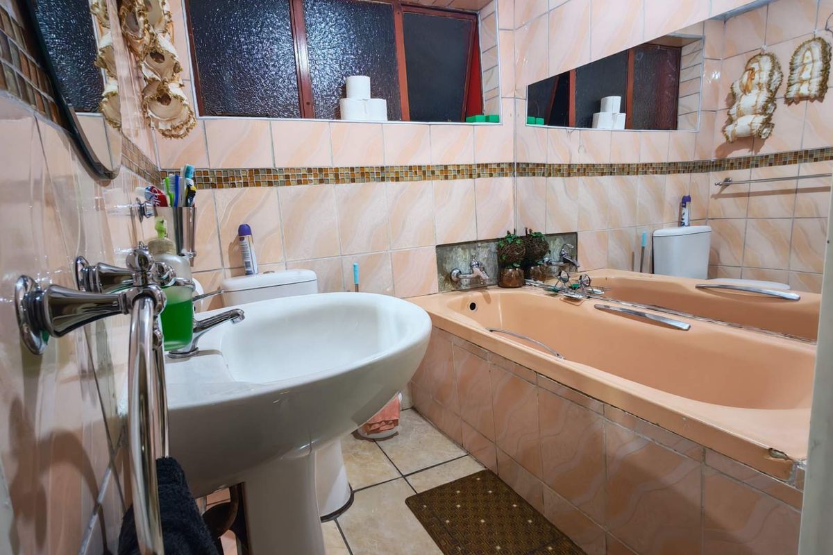 A dated bathroom featuring a peach-toned bathtub, pedestal basin, and tiled walls with a decorative mosaic border.