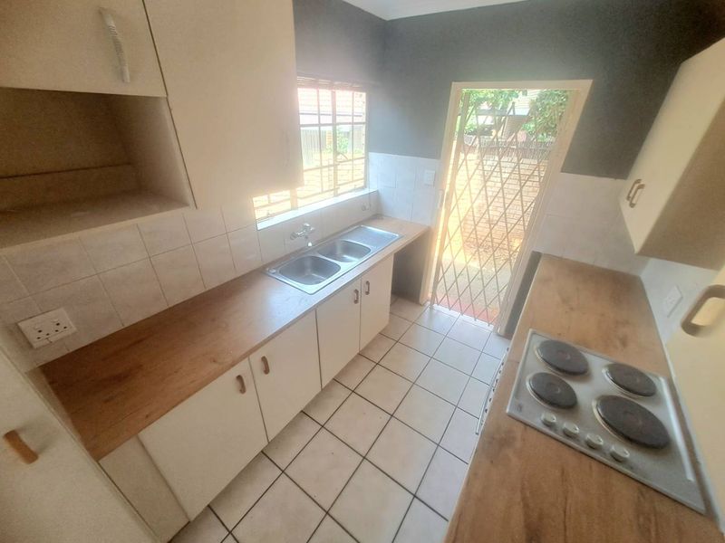 A functional kitchen featuring built-in cabinetry, laminate countertops, a double basin sink, and an electric hob, with direct access to the exterior.