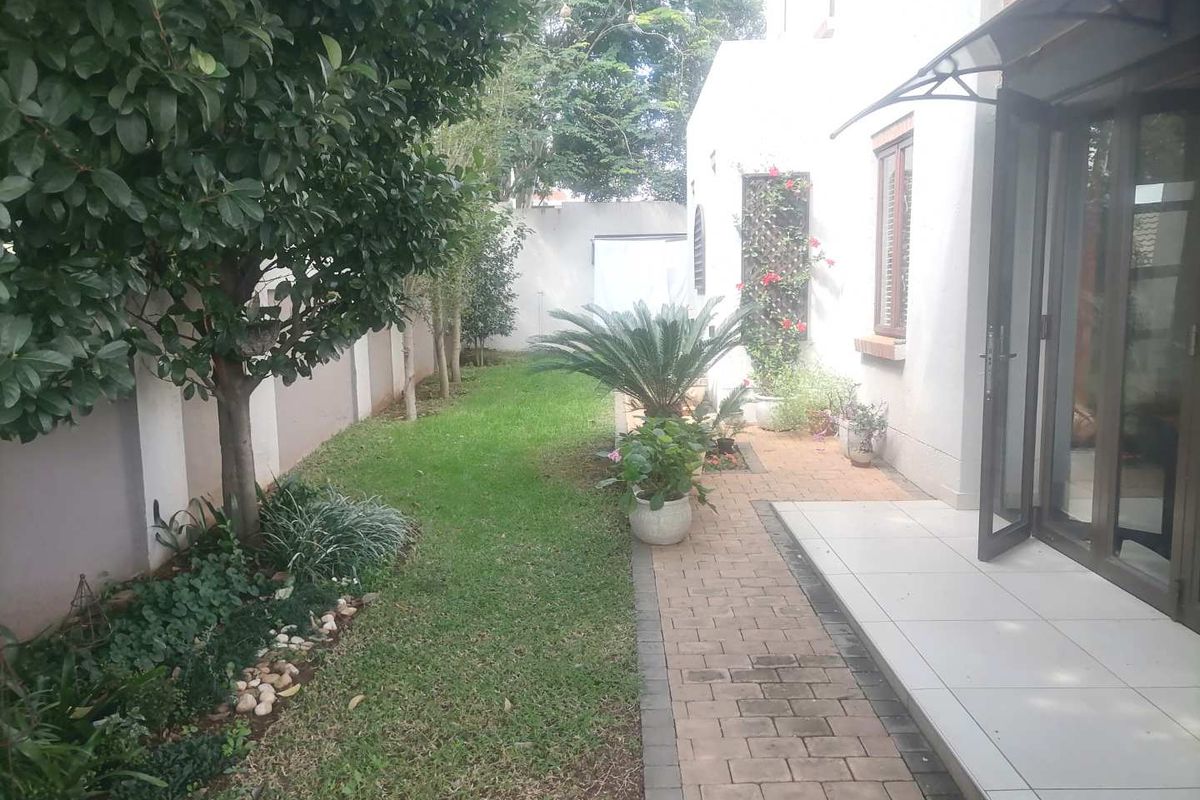 A private rear garden featuring a paved patio area, manicured lawn, perimeter boundary walls, and established garden beds.