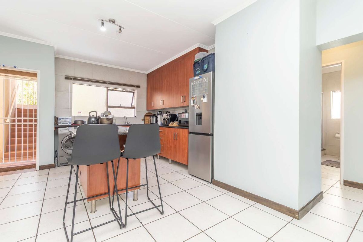 Functional kitchen featuring wood-finish cabinetry, tiled flooring, and a breakfast island, with direct access to an exterior utility area and adjacent bathroom.