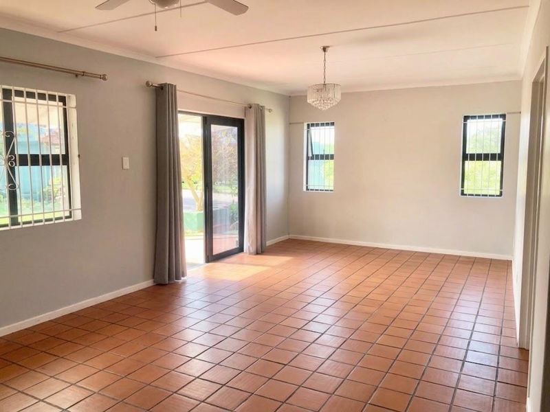 Spacious living area featuring terracotta floor tiles, a ceiling fan, a crystal chandelier, and direct access to the outdoors via a sliding glass door.