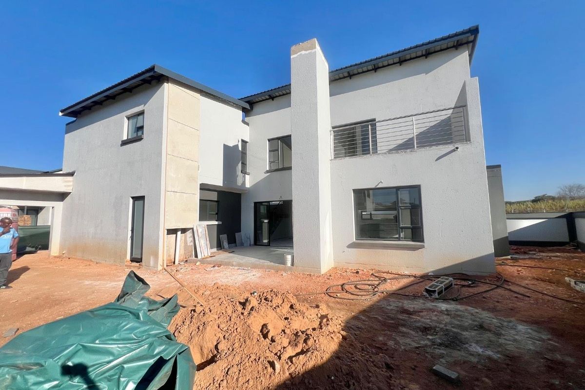 Rear view of a modern double-story cluster home under construction, featuring a chimney stack, balcony, and unfinished outdoor area.