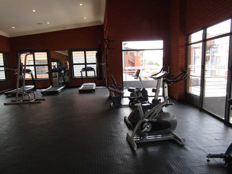 A well-lit, spacious gym area featuring exposed brick walls, durable rubberized flooring, and large windows providing natural light and exterior views.