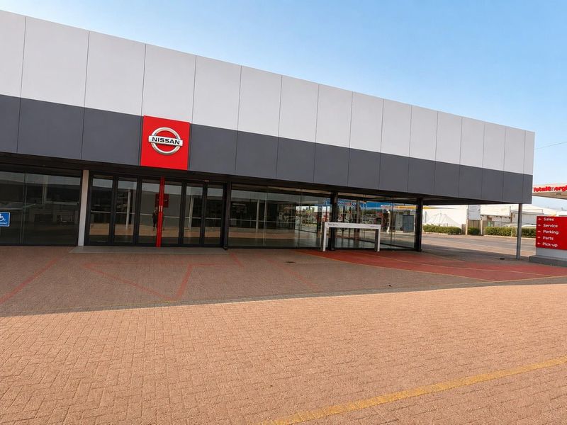 Front elevation of a commercial showroom building featuring a paved forecourt, large glass display windows, and prominent branding signage.