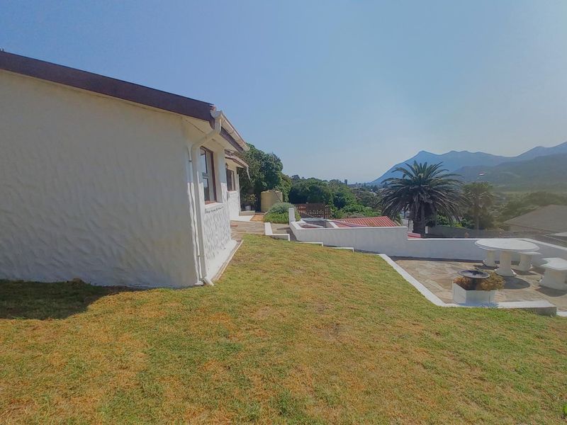 Rear exterior view featuring a paved patio area, lawn, and retaining wall with scenic mountain views in the background.