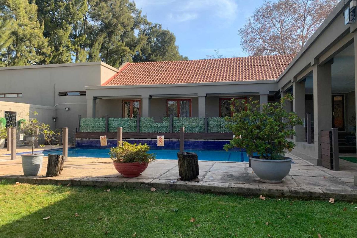 Outdoor pool area featuring a swimming pool with tiled surround, adjacent covered patio, and established garden setting.