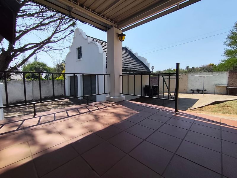 A covered outdoor patio area featuring tiled flooring and metal railings, overlooking a rear garden and a separate outbuilding structure.