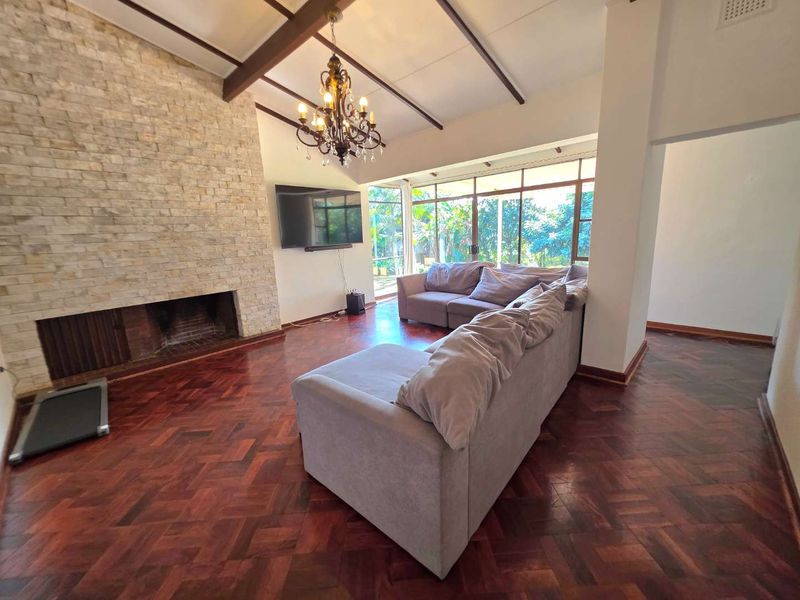 Spacious living room featuring a stone-clad fireplace, exposed timber ceiling beams, and classic parquet flooring with large glass doors leading to the garden.