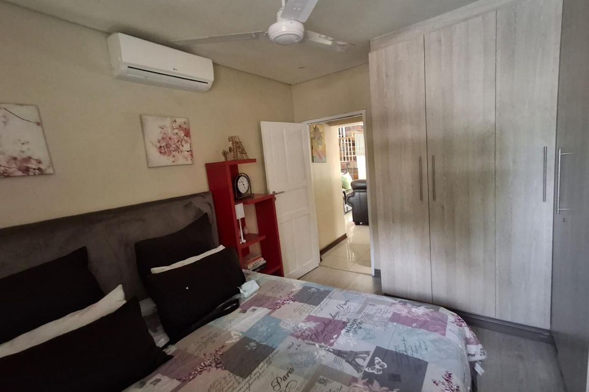 A bedroom featuring built-in wooden wardrobes, a ceiling fan, and a wall-mounted air conditioning unit.