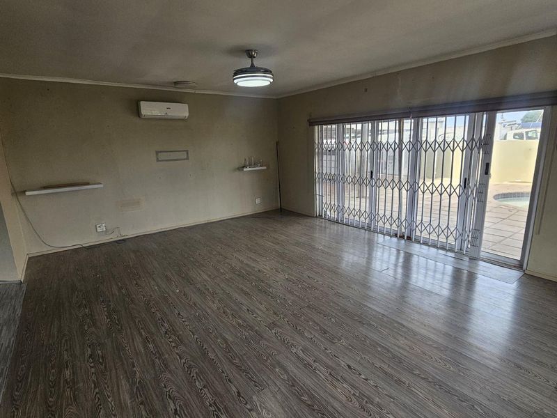 Spacious living area featuring laminate flooring, a split-system air conditioner, and sliding glass doors with security gates leading to the outdoor pool area.
