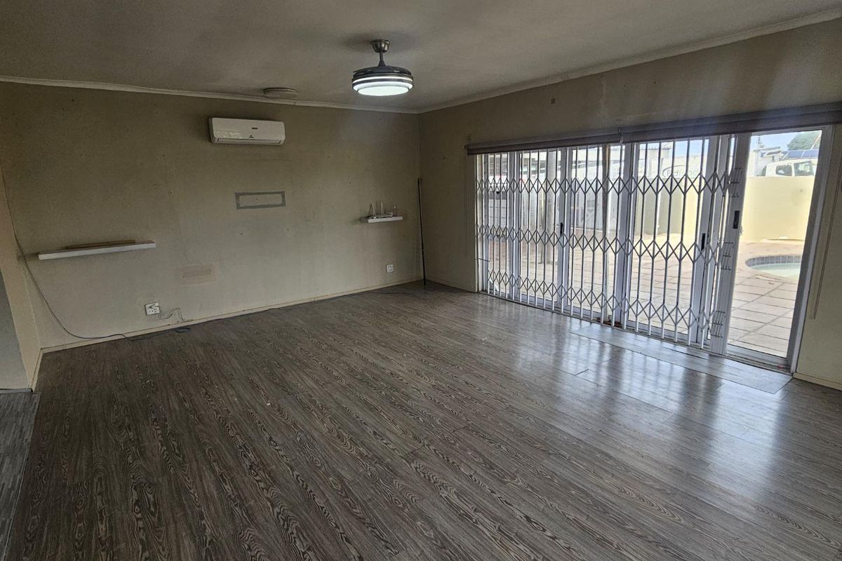 Spacious living area featuring laminate flooring, a split-system air conditioner, and sliding glass doors with security gates leading to the outdoor pool area.