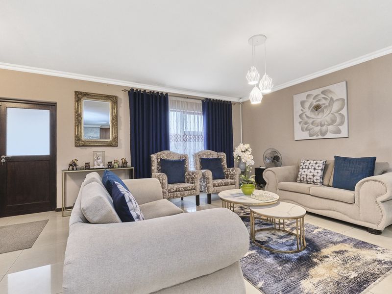 A well-maintained living room featuring neutral tiled flooring, decorative cove cornicing, and modern pendant lighting, creating a comfortable and inviting atmosphere.
