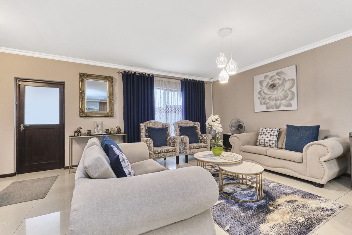 A well-maintained living room featuring neutral tiled flooring, decorative cove cornicing, and modern pendant lighting, creating a comfortable and inviting atmosphere.