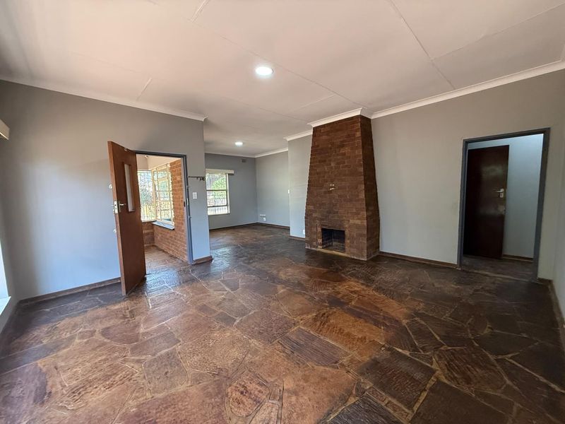 Spacious living area featuring a prominent brick fireplace, unique flagstone flooring, and neutral wall tones, offering a versatile blank canvas for interior design.
