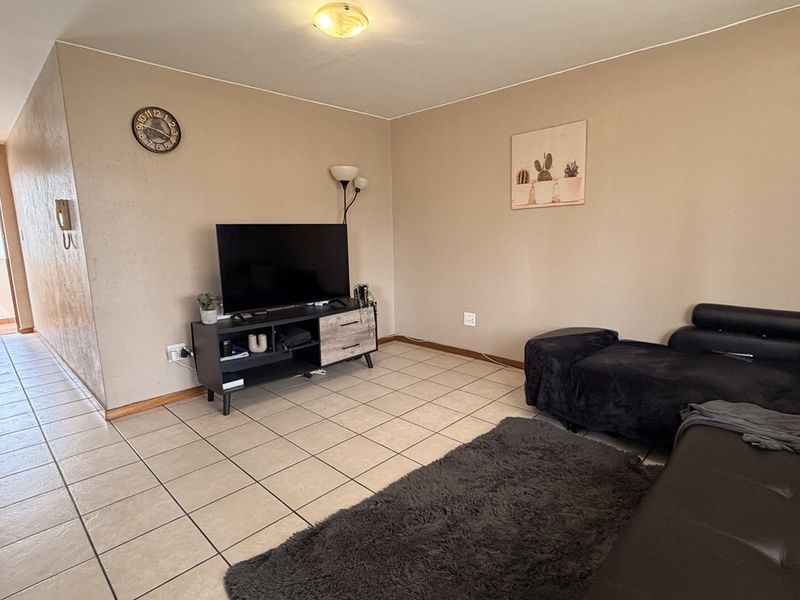 A living room area featuring ceramic floor tiles and neutral wall finishes, providing a functional space with direct access to an adjacent hallway.