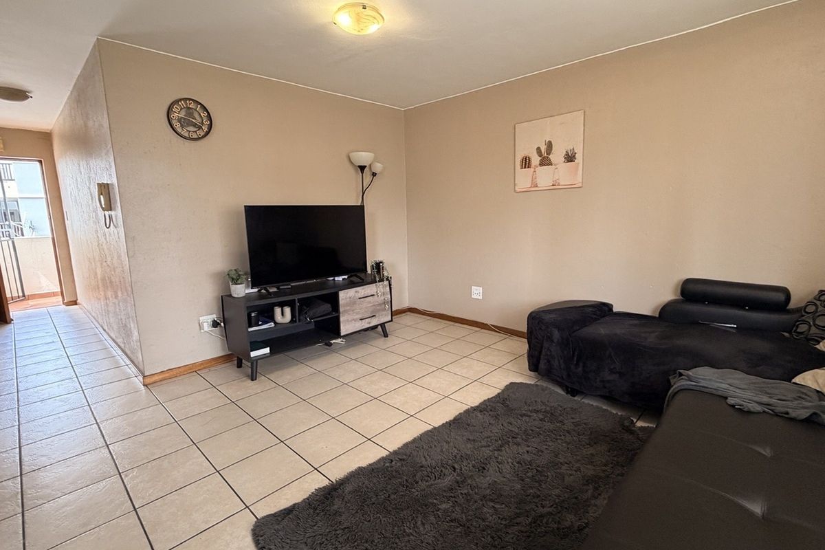 A living room area featuring ceramic floor tiles and neutral wall finishes, providing a functional space with direct access to an adjacent hallway.