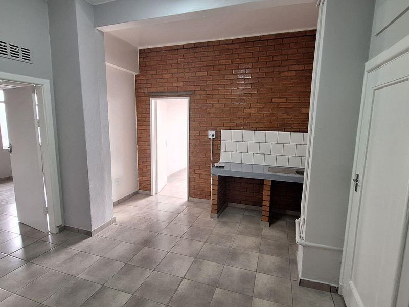 A basic kitchen area featuring exposed brick walls, a simple masonry counter with tiled backsplash, and neutral ceramic floor tiles.