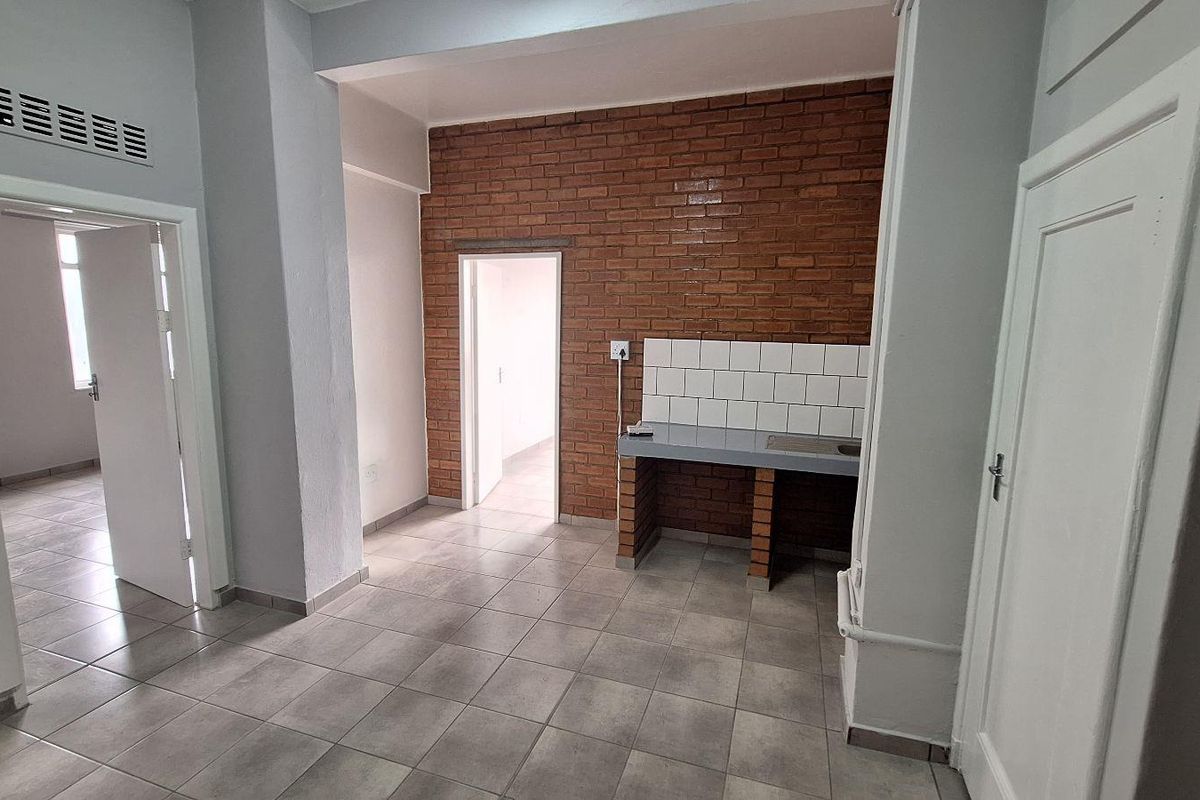 A basic kitchen area featuring exposed brick walls, a simple masonry counter with tiled backsplash, and neutral ceramic floor tiles.
