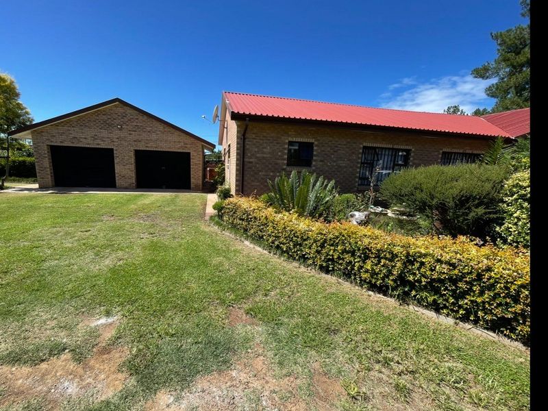 A well-maintained brick house featuring a red metal roof, a double garage, and a neat front garden with established landscaping.