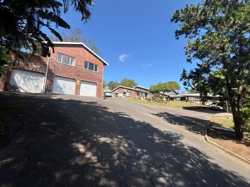 Front view of a brick residential property featuring a large asphalt driveway, double garage, and additional carport parking space.