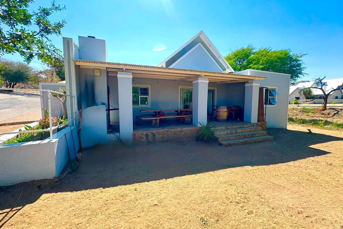 Rear view of the house featuring a covered patio with stone-clad base, concrete pillars, and sliding glass door access.