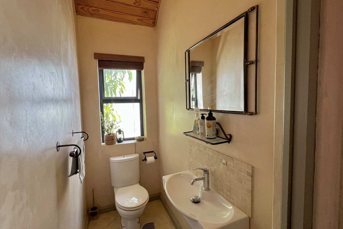 A compact guest bathroom featuring a wall-mounted basin with tiled splashback, a modern toilet, and a distinctive timber-clad ceiling.