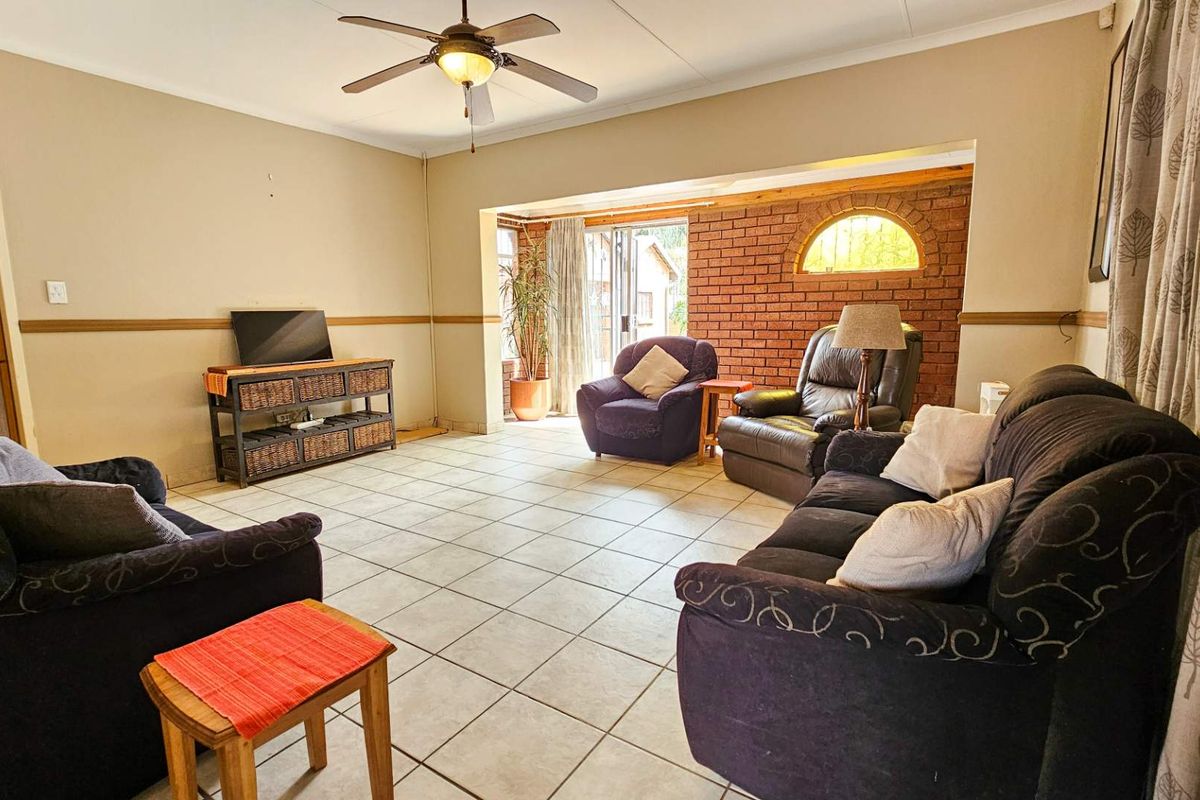 Spacious living room featuring tiled flooring, a ceiling fan, and a distinctive exposed brick feature wall with an arched window detail.