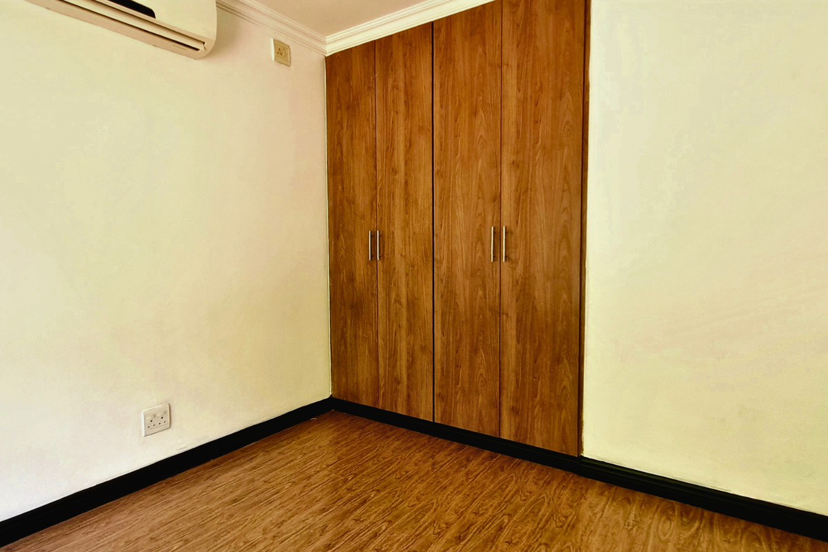 A bedroom featuring wood-look laminate flooring, built-in wooden wardrobes, and a wall-mounted air conditioning unit.
