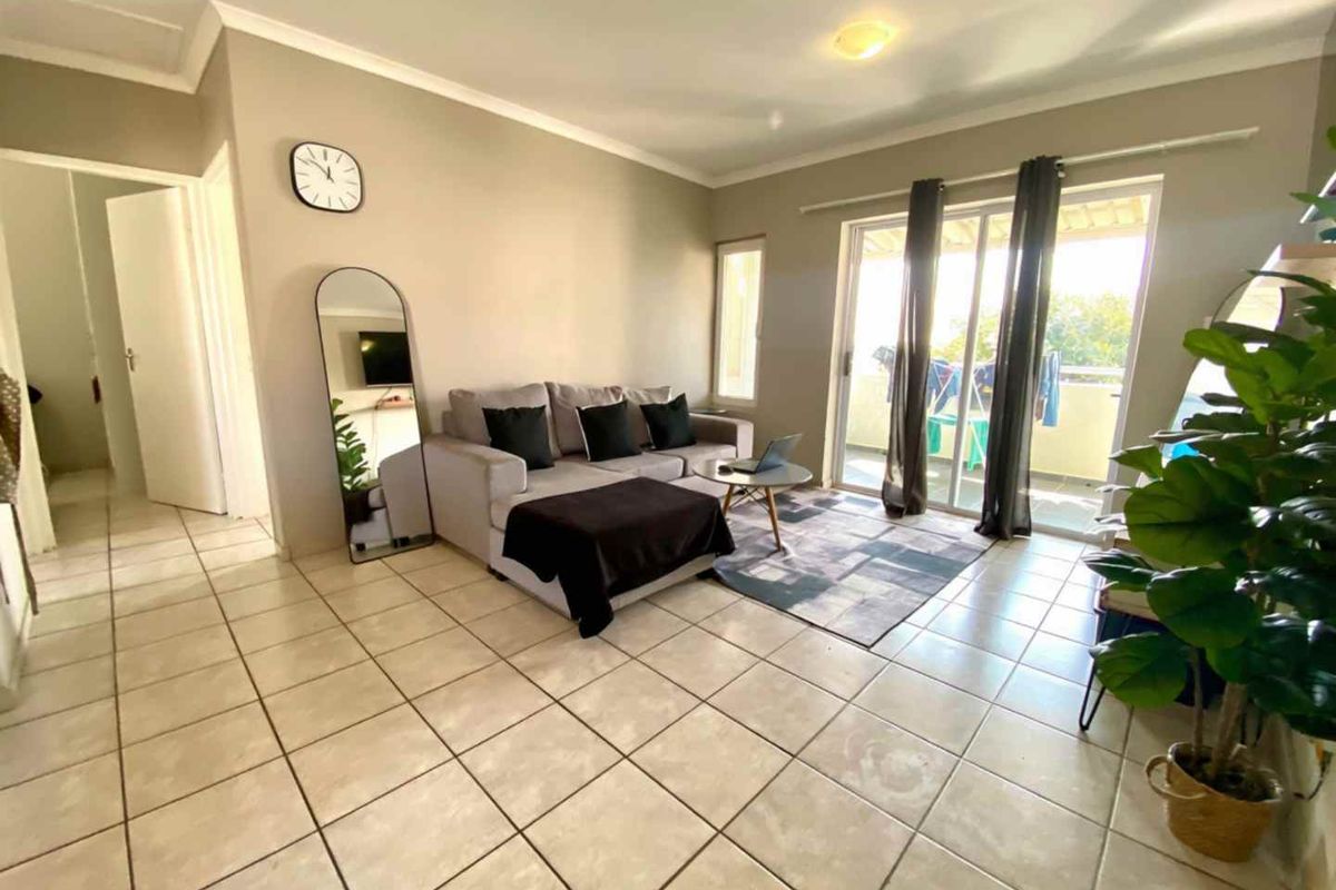 A bright living room featuring neutral tiled flooring and a large sliding glass door providing access to an outdoor balcony area.