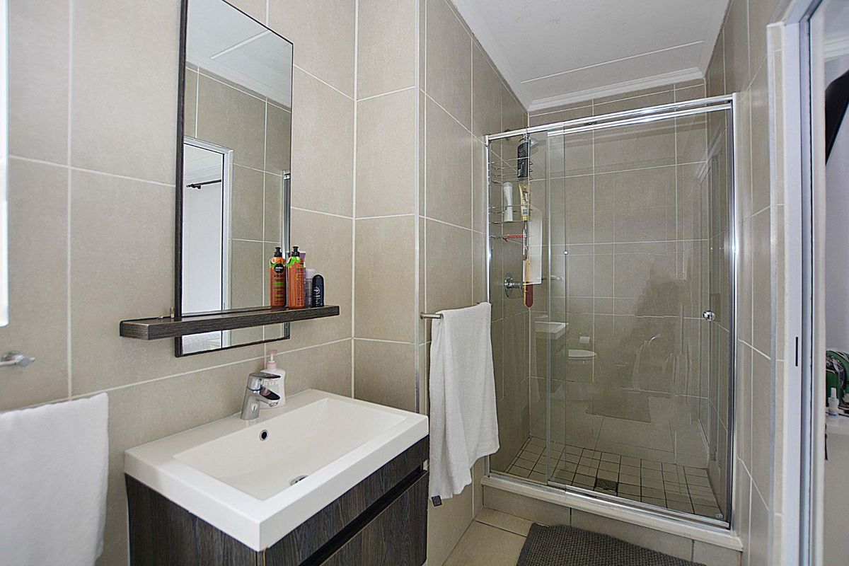 A modern bathroom featuring a vanity cabinet with a ceramic basin, a wall-mounted mirror, and a glass-enclosed shower with neutral wall tiling.