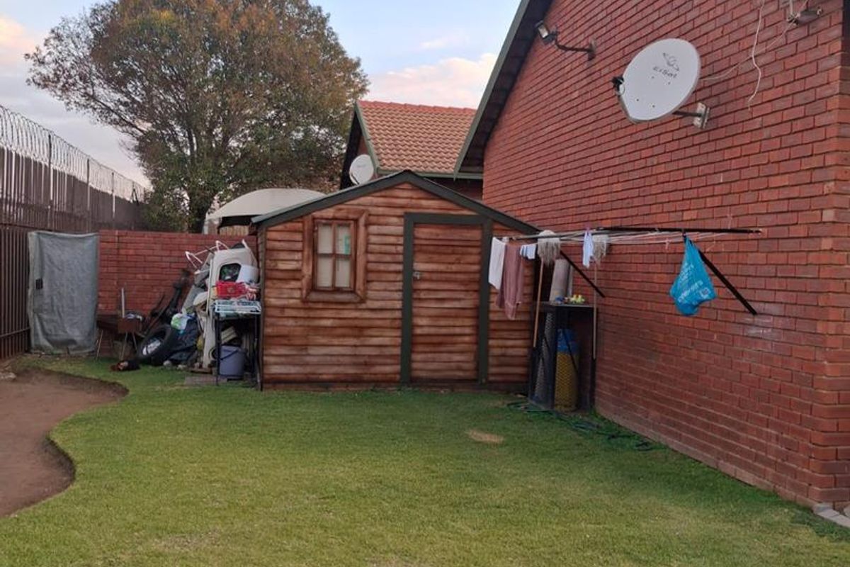 Rear garden area featuring a brick exterior wall, a wooden storage shed, and a wall-mounted washing line.