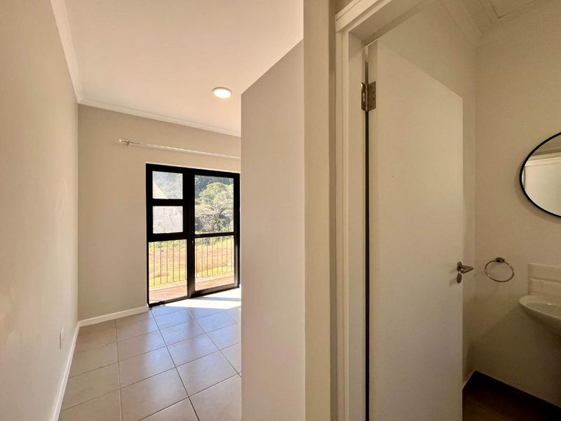 A bright, neutral hallway featuring tiled flooring, recessed lighting, and a glass door leading to an outdoor area, with an adjacent small washroom.