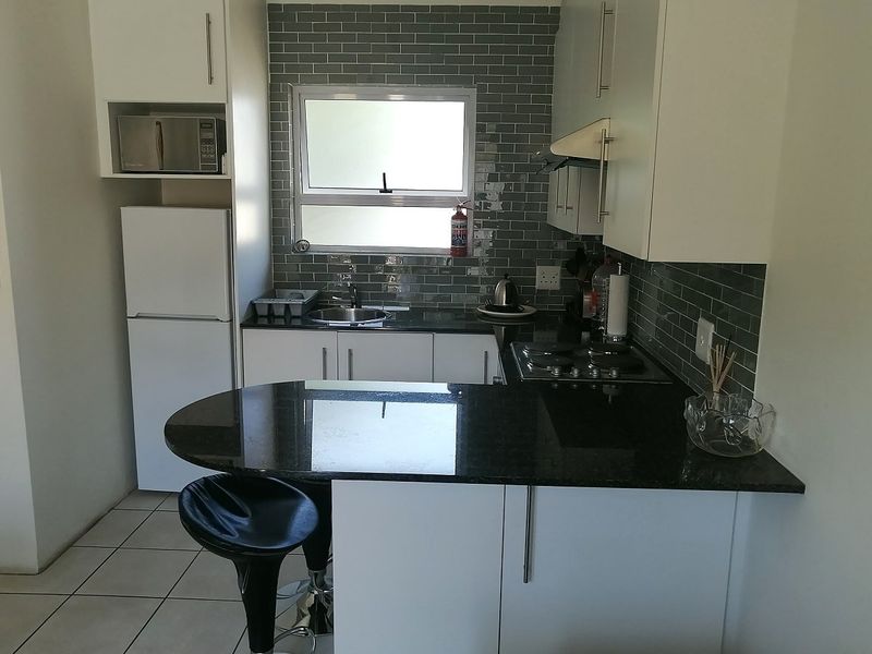 Compact modern kitchen featuring white cabinetry, dark granite countertops, a gas hob, extractor fan, and stylish grey subway tile backsplash.