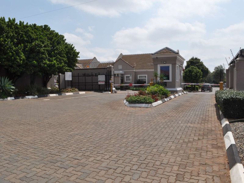 The entrance to the townhouse complex features a secure gated access point with a guard house, paved driveway, and perimeter electric fencing.