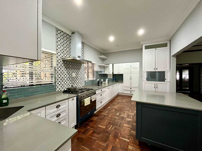 Modern kitchen featuring shaker-style cabinetry, stone countertops, a central island, gas stove with extractor, and elegant parquet flooring.
