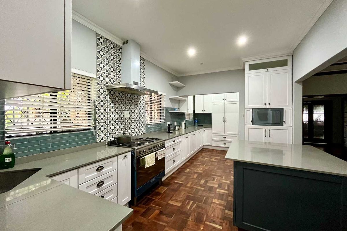 Modern kitchen featuring shaker-style cabinetry, stone countertops, a central island, gas stove with extractor, and elegant parquet flooring.