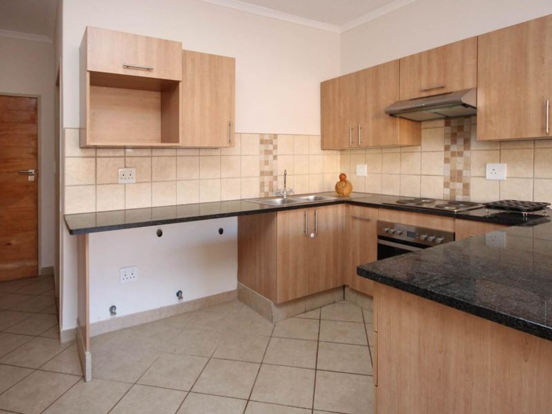 A functional kitchen featuring laminate cabinetry, granite countertops, built-in oven, hob, extractor fan, and tiled flooring.