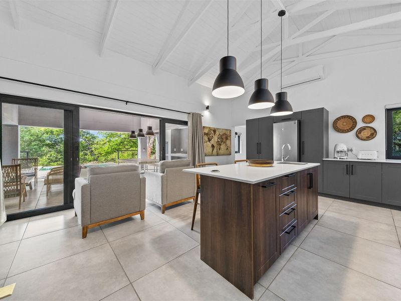 Modern open-plan kitchen and living area featuring a central island, sleek cabinetry, vaulted ceilings, and large sliding doors opening to a patio.