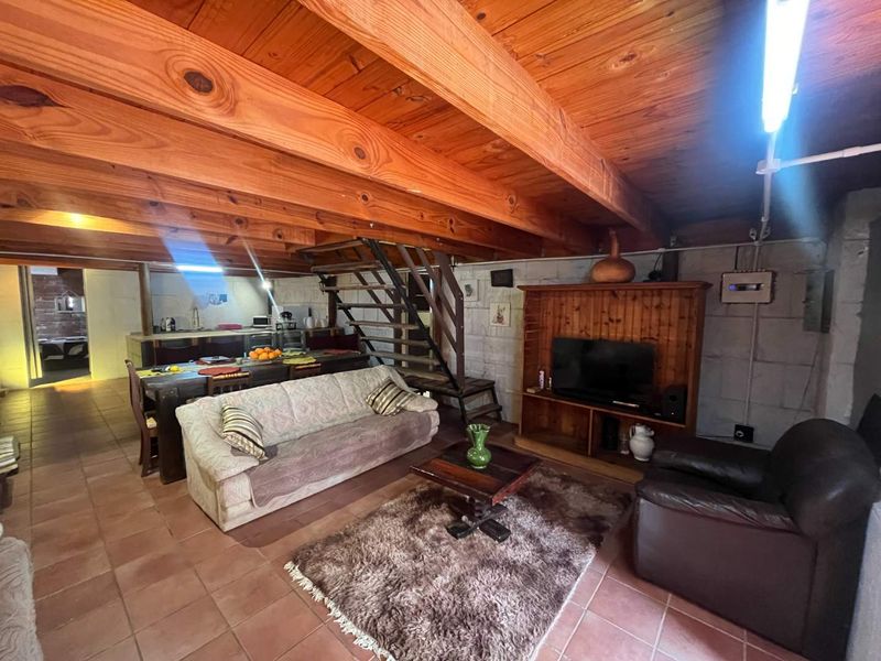 Open-plan living area featuring exposed timber ceiling beams, tiled flooring, and a central timber staircase connecting to the kitchen space.