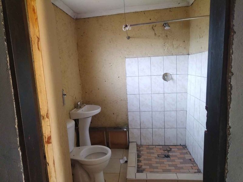 A basic bathroom featuring a pedestal basin, toilet, and tiled shower area, currently requiring significant renovation and cosmetic updates to improve functionality and aesthetics.