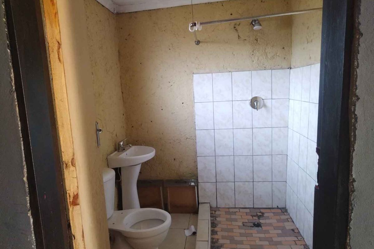 A basic bathroom featuring a pedestal basin, toilet, and tiled shower area, currently requiring significant renovation and cosmetic updates to improve functionality and aesthetics.