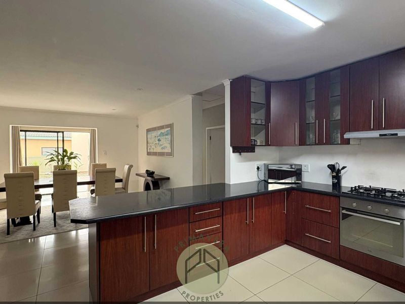Spacious open-plan kitchen and dining area featuring dark wood cabinetry, granite countertops, built-in appliances, and tiled flooring with access to the patio.