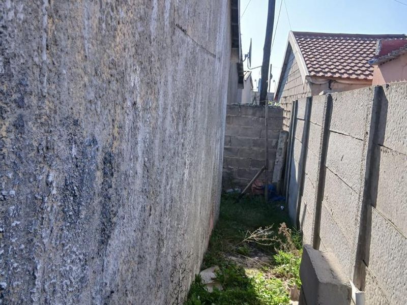 A narrow side passage between the house and a precast concrete boundary wall, showing significant weathering and maintenance requirements.