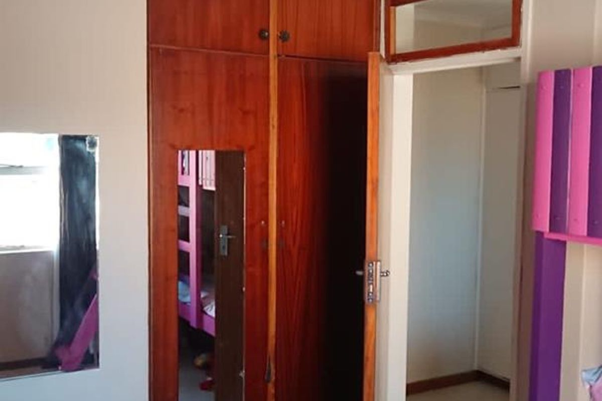 A bedroom featuring built-in wooden cupboards, tiled flooring, and a ceiling fan, with an adjacent doorway leading to a hallway.