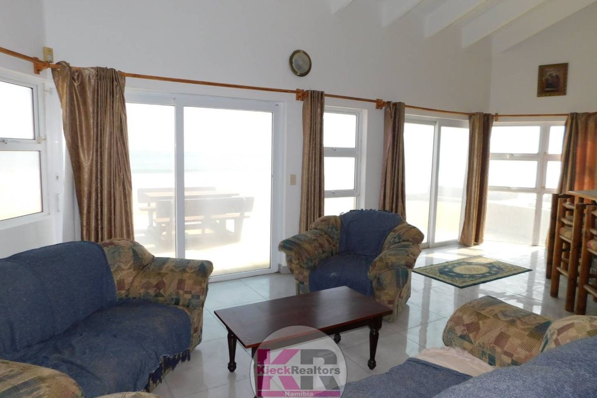 Spacious living room featuring vaulted ceilings with exposed rafters, tiled flooring, and multiple sliding glass doors providing natural light and access to the outdoors.