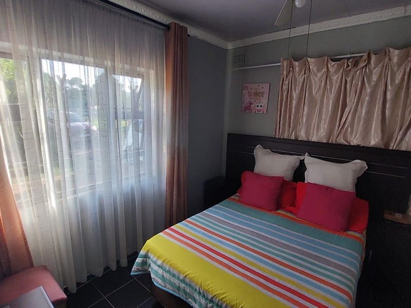 A functional bedroom featuring tiled flooring, ceiling cornicing, and a large window allowing natural light.